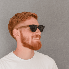 hombre joven de piel blanca y pelo rojo con anteojos de sol de acetato negro y patillas de madera de forma redonda modelo Copenhague marca Nomade