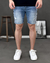 Homem usando shorts jeans claros com detalhes rasgados, combinado com tênis brancos.