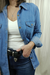 Mujer vistiendo una camisa de jean azul con una camiseta blanca y jeans, mientras se apoya en su cadera. La camisa se vende en este sitio web.