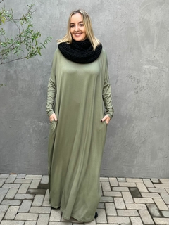 vestido longo, bem amplo, na cor verde militar, tem um estilo despojado, a modelo usa uma gola de tricot preta para deixar o look mais elegante