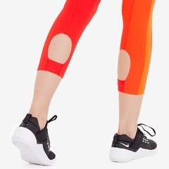 Calzas Nike Running para mujer en color rojo y naranja, con detalles en las rodillas y calzado deportivo negro.