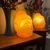 luminaria-mesa-bivolt-formato-cabeca-buda-laranja-em-cima-mesa-acesa-lado