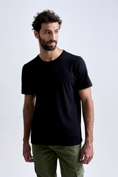 Camiseta preta modelo masculino, com corte clássico, combinada com calças verdes.