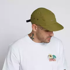 Homem usando um boné verde oliváceo com logotipo da RVCA e camiseta branca com estampa colorida.