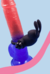 Coelhito anel peniano vibrador em visão de trás, mostrando sua funcionalidade de vibração com orelhas que estimulam o clitoris em fundo azul e rosa.