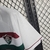 A camisa reserva do Fluminense II para a temporada 23/24 é predominantemente branca. Apresenta duas faixas horizontais no peito, uma em grená e outra em verde, acompanhadas de uma linha grená na parte inferior. A gola em formato de V é branca, com detalhe