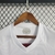 A camisa reserva do Fluminense II para a temporada 23/24 é predominantemente branca. Apresenta duas faixas horizontais no peito, uma em grená e outra em verde, acompanhadas de uma linha grená na parte inferior. A gola em formato de V é branca, com detalhe
