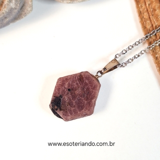 Colar com pedra rubi bruto, destacando sua cor rosa e formato hexagonal, pendurado em corrente de metal.