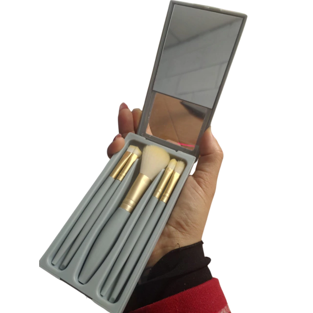 Conjunto de pincéis de maquiagem com espelho em uma embalagem compacta, segurado por uma mão.