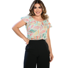 Mulher sorridente vestindo uma blusa estampada com folhas coloridas e calças pretas.