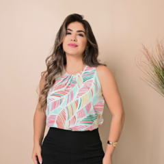 Mulher com blusa estampada de folhas coloridas e saia preta, posando em fundo neutro.