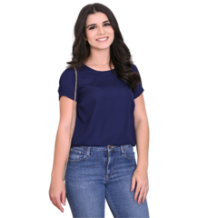 Mulher sorrindo, vestindo uma blusa azul marinho e jeans, em fundo branco.