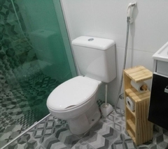 Banheiro moderno com vaso sanitário e porta papel higiênico de madeira.