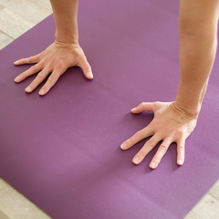 Manos apoyadas sobre un mat de yoga violeta, antideslizante y para prácticas intensas. 