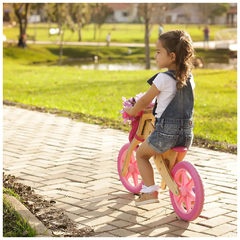 Menina andando de bicicleta de madeira sem pedal rosa