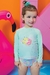 Menina sorridente usando um conjunto de blusa e calcinha em malha com proteção UV 50+, com estampa colorida e detalhes florais, ao lado de um flamingo inflável.