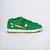 O tênis Nike Dunk Low SB St. Patrick's Day é um modelo masculino com um visual marcante, sendo predominantemente verde com detalhes em dourado no swoosh. O material é uma combinação de camurça e tecido, e o tipo de ajuste é por cadarços. Este modelo está 