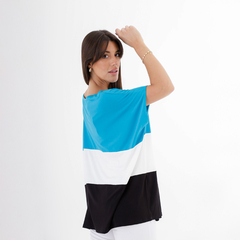 Una mujer viste un remerón de colores azul, blanco y negro, con un diseño moderno, mostrando la espalda y levantando una mano.