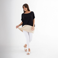 Mujer luciendo un remerón Puglia de color negro con un diseño de parte inferior beige, combinándolo con pantalones blancos y sandalias.