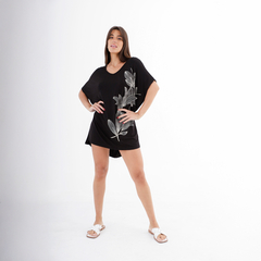 Mujer posando con una camiseta negra de estilo suelto con estampado de hojas en un fondo blanco.