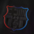 Camisa reserva do Barcelona 2024-2025 da Nike. A peça apresenta a cor preta como predominante, com o escudo do clube aplicado em TPU com efeito brilhante no centro. O Swoosh da Nike aparece com contorno degradê azul e vermelho. A gola é estilo "mini-polo"