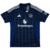 nova camisa reserva do Manchester United para a temporada 2024-2025. A camisa, predominantemente azul, possui um padrão de letras "M" formando diamantes brilhantes e detalhes em branco, incluindo as três listras da Adidas nas mangas e o escudo do clube no