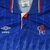 Camisa retrô Chelsea Umbro 1989-1991 em azul marinho, vermelha e branca. Usada na última temporada de Bobby Campbell, destacando-se nas semifinais da Rumbelows Cup e posição sólida na Division One.