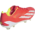 chuteira de campo adidas X Crazyfast+ FG Energy Citrus. A chuteira possui um cabedal vermelho vibrante (Solar Red) com listras e suporte do calcanhar brancos (Cloud White). Detalhes em amarelo neon (Solar Yellow) aparecem no interior do calçado e na placa