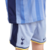 Conjunto infantil do Tottenham 2024-25: camisa azul claro com faixas verticais em tons variados, gola V assimétrica e punhos em azul marinho, amarelo e branco. Escudo centralizado e logo Nike em azul marinho. Shorts azul claro com detalhes em azul complet