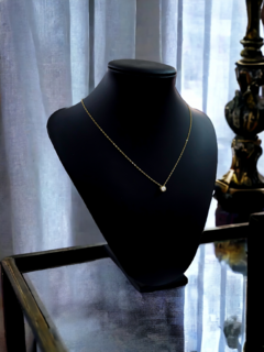 Collar delicado de oro con un pequeño colgante brillante exhibido en un maniquí negro.