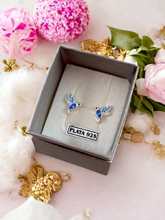 Aros de plata con diseño de colibrí en tonos azules, presentados en una caja gris con la etiqueta de PLATA 925.