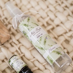Frasco transparente de spray para ambientes de aroma Alecrim, da marca Mels Brushes, produto sobre cesto de palha.
