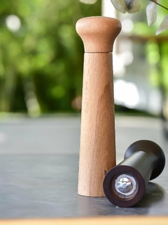 um moedor de pimenta de madeira clara sobre uma mesa e um moedor de pimenta de madeira escura do lado mostrando o mecanismo de moagem
