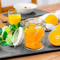Um pote de vidro hermético aberto, cheia de laranjas em cima de uma mesa