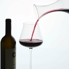 um decanter enchendo uma taça de vinho e uma garrafa de vinho