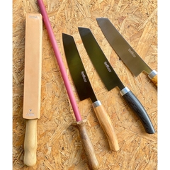 um afiador de couro strop, uma chaira de afiar facas e três facas sobre uma mesa de madeira
