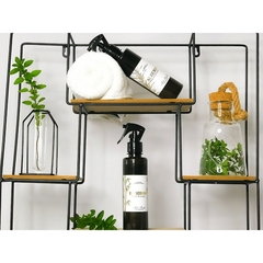Dois frascos âmbar com home spray de ambientes e água de tecidos aroma alecrim da marca Mels Brushes sobre estante em madeira ladeado por vasos com plantas verdes.