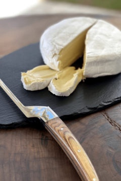 uma faca para queijo macio em cima de uma tábua de ardósia com um queijo brie cortado