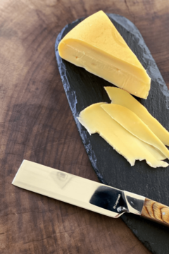 uma faca para queijo ao lado de uma tábua de ardósia com um pedaço de queijo