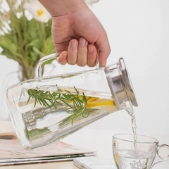 uma pessoa segurando uma jarra de vidro com tampa de inox com água saborizada e servindo em um copo
