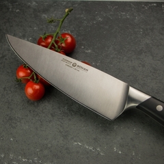 Uma faca de cozinha, com lâmina de aço inox e cabo preto, em cima de um balcão ao lado de tomates.