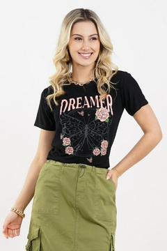 Modelo loira usando uma camiseta preta com estampa de borboleta com rosas e a palavra "DREAMER". Posando sobre um fundo branco. G&B Bros!