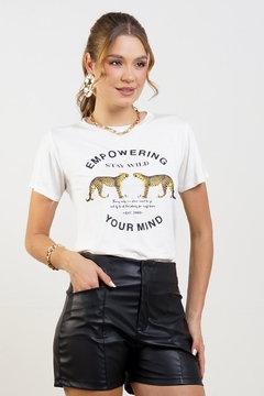 Modelo loira usando uma camiseta na cor off white com estampa de duas onças se encarando e a frase Empowering your mind. Fazendo pose sobre um fundo branco. G&B Bros.