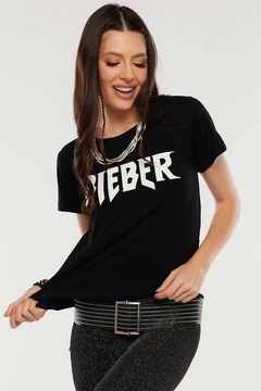 Modelo morena usando uma camiseta preta com a estampa simples escrita Bieber com letras brancas, olhando para baixo e sorrindo, segurando a barra da camiseta com as mãos, sobre um fundo branco. G&B Bros!