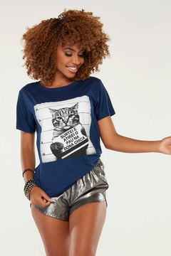 Modelo afrodescendente de cabelo crespo usando uma camiseta na cor azul marinho com a estampa do gato dona chica, fazendo pose sobre um fundo branco e sorrindo. G&B Bros!