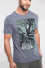 O modelo veste uma camiseta de manga curta cinza com uma estampa no tórax, trata-se de uma ilustração da copa de uma árvore visto por baixo, as luzes do sol iluminando as frechas que se formam entre folhas verdes.