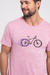 O modelo veste uma camiseta de manga curta rosa com uma estampa no tórax, trata-se da uma ilustração de uma bicicleta em movimento, as rodas traseiras emitem um neon lilás.