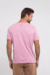 O modelo veste uma camiseta de manga curta rosa com uma estampa no tórax, trata-se de uma ilustração de três folha em sobreposição,  uma delas é verde, as outras duas são pretas.