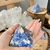 "Handheld Sodalite Pyramid with Clear Quartz Crystals: Personal Clarity and Insight"

In this captivating image, a Sodalite pyramid rests gently in the palm of a woman's hand, surrounded by Clear Quartz crystals. This composition symbolizes personal clari