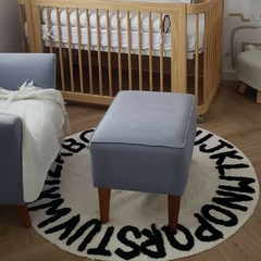tapete infantil redondo alfabeto branco com letras pretas em um quarto de bebê com poltrona e berço ao fundo